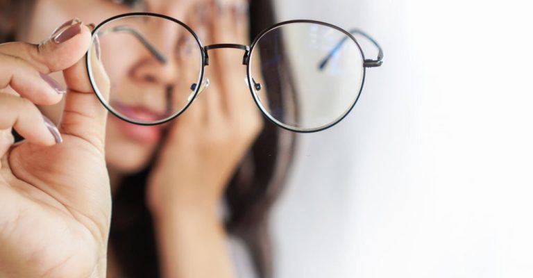 Asian woman hand holding eyeglasses having problem with eye pain, blur vision