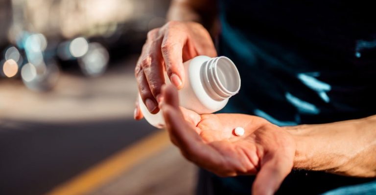 Close up of human hands. Man holding the medicine bottle in one hand and pill in other