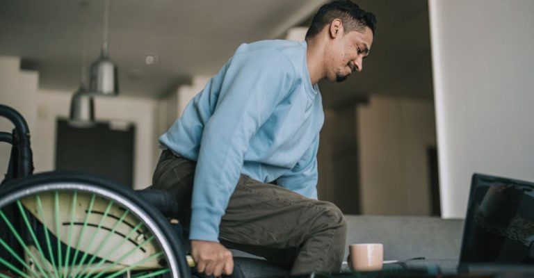 Asian indian with disability getting up from wheelchair and sitting on sofa