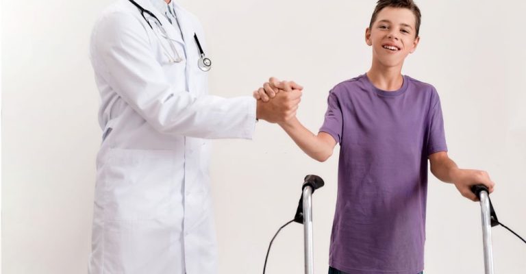 Cropped shot of male doctor shaking hands with teenaged disabled boy with cerebral palsy, taking steps using his walker isolated over white background. Children with disabilities and special needs